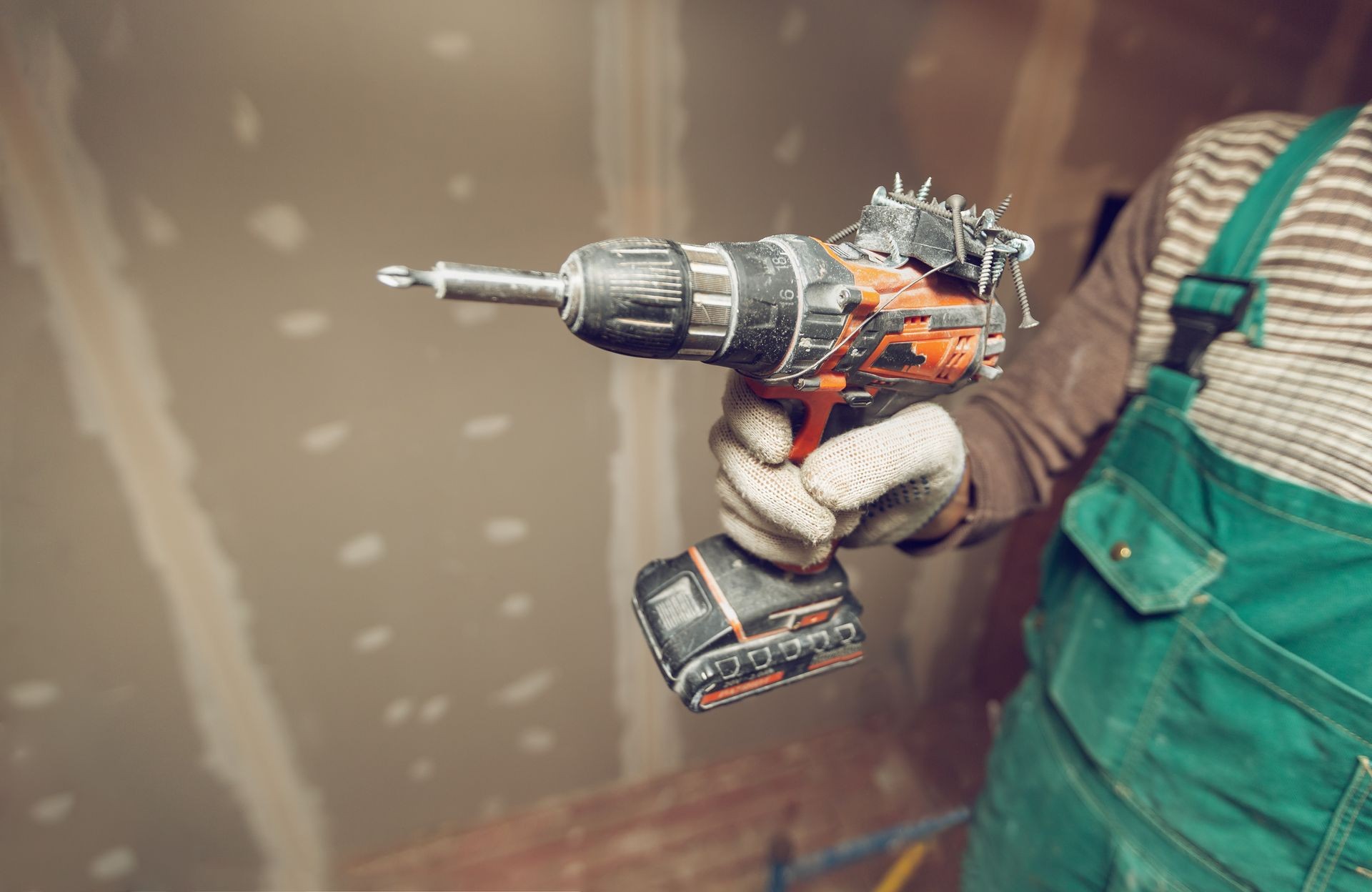 Worker with protective gloves is holdind a drill in apartment that is under construction, remodeling, renovation, overhaul, extension, restoration and reconstruction. Concept of total home improvement